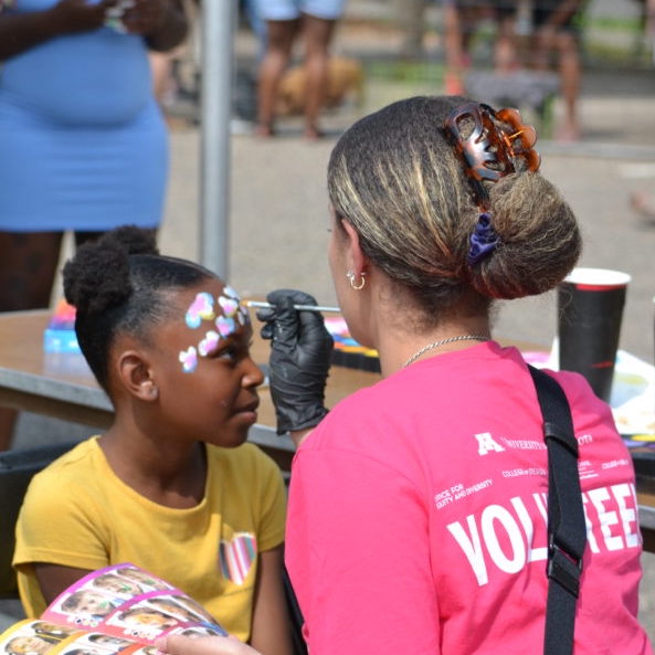 Image of a young black girl having her face painted by a Juneteenth volunteer.